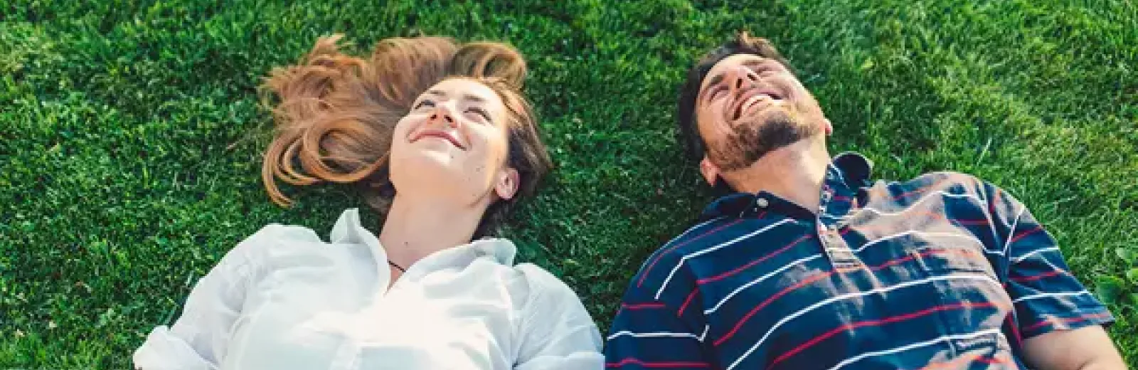 couple laying in plush green healthy grass smiling and laughing