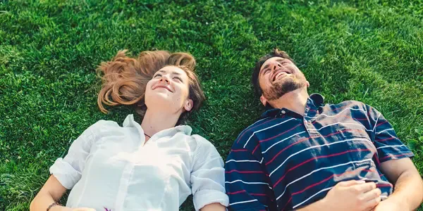 couple laying in plush green healthy grass smiling and laughing